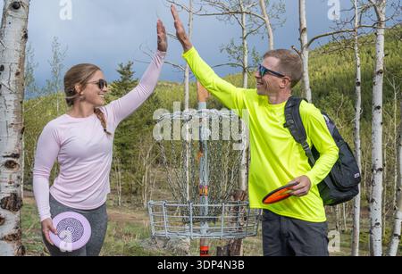 Smiling couple giving high five while playing disc golf in a forest Stock Photo