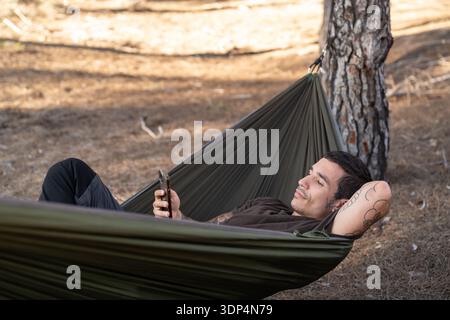 Man relaxing in hammock using smartphone in nature Stock Photo