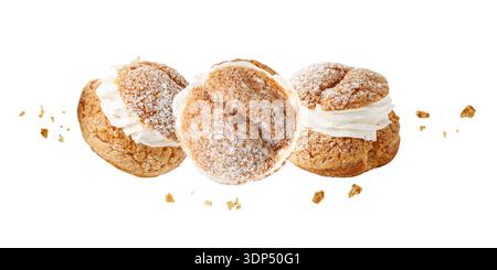 Cream puffs, pastry from choux covered sugar powder with crumbs flying isolated on white background. Sweet dessert for coffee break or party. Stock Photo
