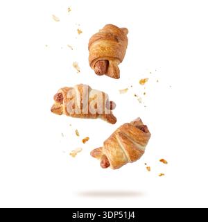 Buttery croissants with sausage and crumbs flying falling isolated on white background. Crusty sausage croissant roll as tasty snack. Stock Photo