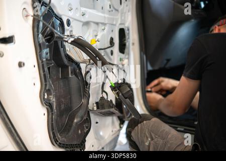 A mechanic is working on the internal wiring of a car door with the panel removed in an automotive repair shop. Stock Photo
