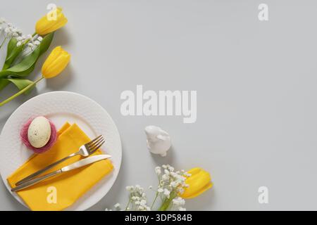 Easter composition with plate, decorative egg, yellow napkin and spring flowers on minimal background with copy space. Stock Photo