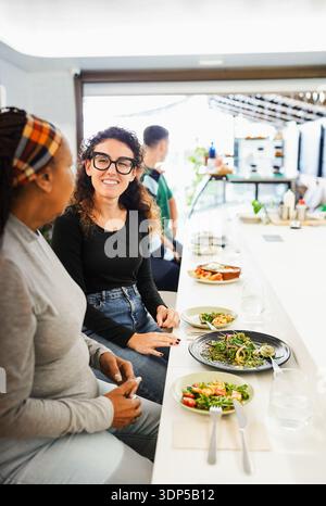 Women friends eating together at lunch time at bistro counter - Multiracial people having fun chatting inside restaurant - Food and healthy lifestyle Stock Photo