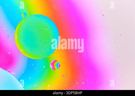 Dynamic macro photography featuring large green blue oil bubble and smaller rainbow colored bubble suspended in pink liquid environment Stock Photo