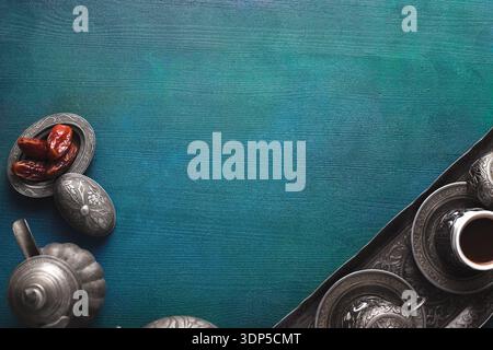 A tray with a cup of coffee, a small plate of dates, and a coffee pot on  blue-green painted wooden table. Top view. Ramadan background. Stock Photo
