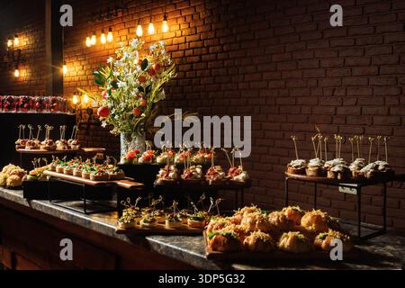 Opulent catering display featuring berry shot glasses, assorted mini tarts, golden-dusted profiteroles and tiered gourmet appetizers Stock Photo