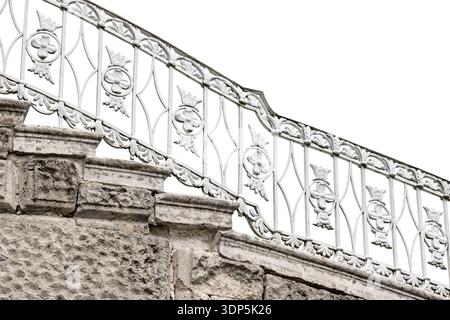 Ornate white wrought iron railing crowns weathered stone steps, highlighting vintage decorative patterns, textured masonry, architectural details. Out Stock Photo