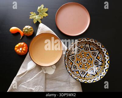 Multicolored ceramic plates and patterned bowl on black background. Design mockup. Food and traditional cuisine. Top view. Stock Photo