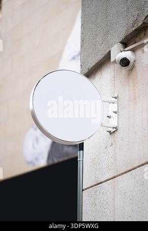 Blank circular outdoor sign mockup mounted on a wall with security camera Stock Photo