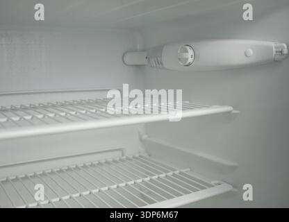 Clean empty fridge interior with adjustable thermostat dial and wire shelves. White modern refrigerator inside view, cold storage concept, minimal kit Stock Photo