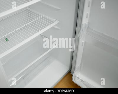 Open empty fridge with wire shelves and transparent door bins. Clean white refrigerator interior, modern kitchen appliance, cold storage concept with Stock Photo