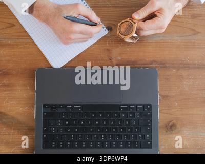 Top view of male hands writing notes at a wooden desk with keyboard. Minimal composition with copy space, concept of work and organization. Stock Photo