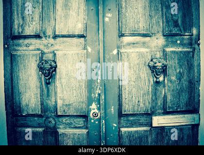 Antique doors. Weathered wooden old door with decorative handles - in shape of human head with wreath on it (like Roman patrician). Paris, France. Blu Stock Photo