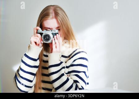 Stylish woman holding vintage camera in her hand in bright sunlight. Photography passion, creative hobby and retro technology concept with copy space. Stock Photo