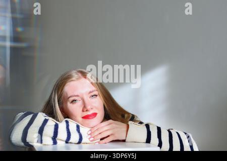 Thoughtful blonde woman with red lips relaxing indoors, copy space Stock Photo