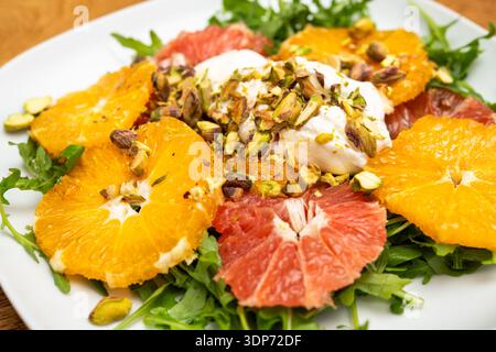 Fresh sliced oranges and grapefruit served on arugula with a dollop of cream and sprinkled with chopped pistachios on a white plate. Stock Photo