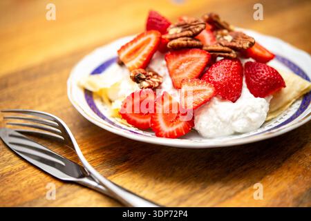 A plate with sliced strawberries, pecans, and cottage cheese on a wooden table with two forks next to it is shown in closeup. Stock Photo