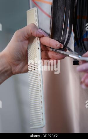 Close-up of a hairdressers hands using scissors and a comb to cut and style dark hair, showcasing precision and care in a salon setting. High quality Stock Photo
