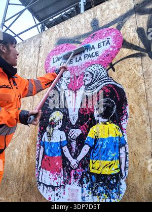 Milan, love is as ageless as peace. A work by CDonati Meyer for a peaceful Valentine's Day. For Valentine's Day, a street art project that combines visual language and civic engagement in a universal message. Created in graffiti style with a palette of fuchsia, black, and white, the work depicts an elderly couple-an Israeli man and a Palestinian woman-holding hands beneath a large heart covered in drippings and splashes of color. In front of them, two children-a girl in the colors of Russia and a boy in those of Ukraine-also hold hands. Stock Photo
