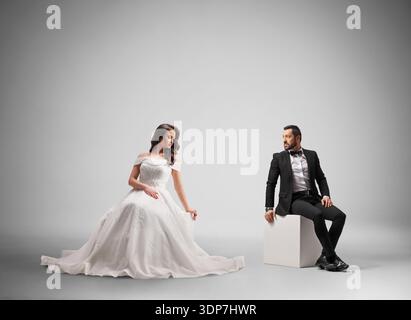 Bride and groom sitting and looking at each other in a studio Stock Photo