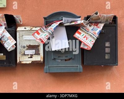 Overflowing mailboxes on a terracotta wall in Catania, Italy. Letterboxes clogged with advertising flyers, junk mail, and newspapers. Residential comm Stock Photo