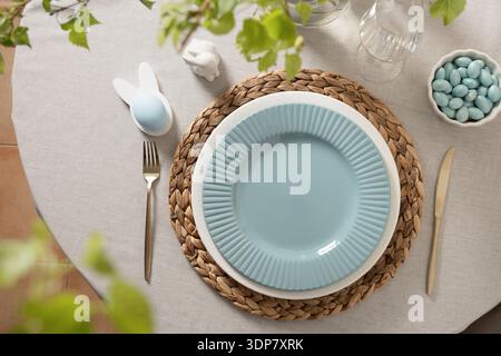 Spring Easter table arrangement with ceramic plates, bunny egg decoration and golden cutlery on neutral textile background with copy space. Stock Photo