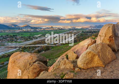 Elevated landscape view from Mt Rubidoux Trail overlooks the city of Riverside, California, featuring large boulders and dramatic golden sunset clouds Stock Photo