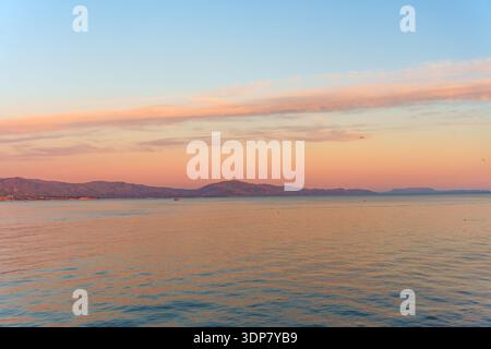 Serene and minimalist seascape featuring soft, pastel pink clouds stretching over a calm ocean, creating a peaceful and meditative mood at dusk. Stock Photo