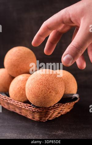 Vertical shot of golden round buns arranged in a wicker basket with a hand reaching to pick one, highlighting fresh-baked texture and warm, appetizing Stock Photo
