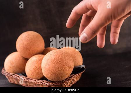 Golden round buns arranged in a wicker basket with a hand reaching to pick one, highlighting fresh-baked texture and warm, appetizing appeal for baker Stock Photo