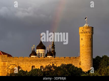 Medieval stone castle wall with round tower and flag, onion-domed cathedral spires behind, dramatic storm clouds and faint rainbow at golden hour; tre Stock Photo