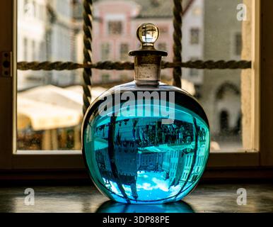 Blue glass bottle on a windowsill reflects an upside-down city street scene through a pane with iron bars, creating a surreal, vintage still life with Stock Photo