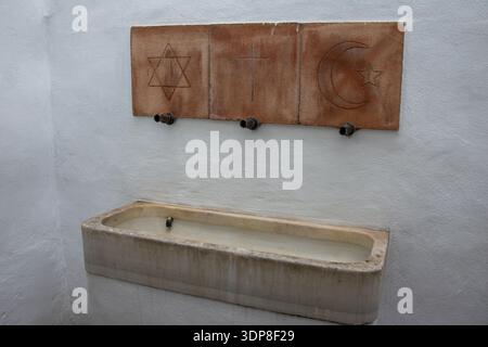 Fuente pública con azulejos tradicionales que representan símbolos de diferentes religiones sobre una pared encalada en  Frigiliana, Andalucía, España Stock Photo