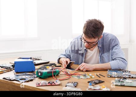 Technician Works on Circuit Board Repairs at a Cluttered Table in Bright Indoor Space Stock Photo