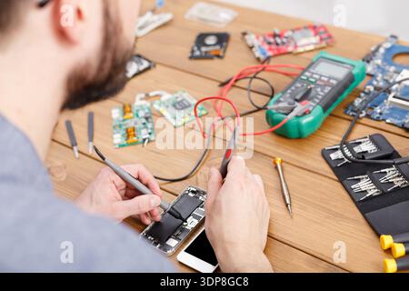 Technician Repairs Smartphone on Wooden Table With Tools and Circuit Boards Stock Photo