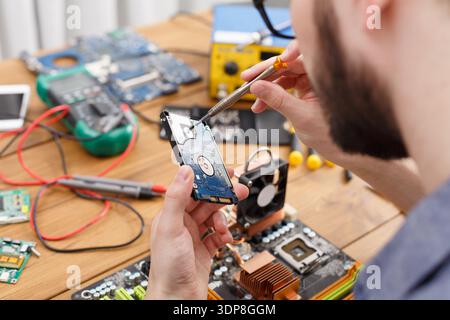 Man Repairs Hard Drive in a Workshop With Various Electrical Tools and Gadgets Around Him Stock Photo