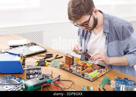 Young Man Repairs Computer Motherboard at a Workspace With Tools and Devices During the Day Stock Photo