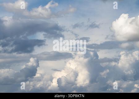 Dramatic layered cumulus clouds dominate an overcast sky with bright sunlit highlights and blue gaps, creating a moody, textured atmosphere suitable f Stock Photo
