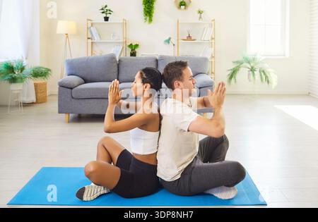 Couple meditating back to back at home on yoga mat in mindfulness together Stock Photo