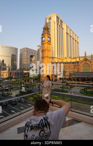 A photographer captures a portrait of a woman in front of the life-size Elizabeth Tower (Big Ben replica) at The Londoner Macao during sunset. Stock Photo