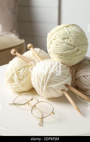 Knitting yarns, needles and glasses on white table at home, closeup Stock Photo