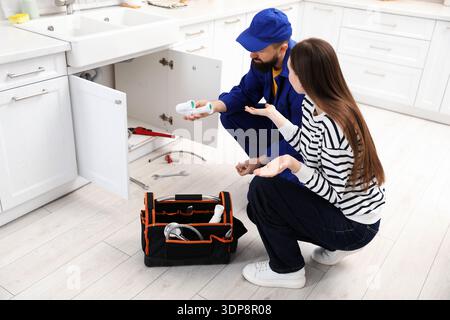 Young woman talking with plumber in kitchen Stock Photo