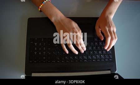 Focused individual operating laptop keyboard. Person typing on laptop with beaded bracelet Stock Photo