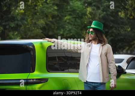 Happy handsome caucasian man in festive green costume standing near car celebrating St Patrick day. Stock Photo