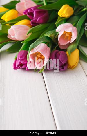 Colorful Bouquet of Tulips on a White Wooden Surface in a Bright Setting Stock Photo