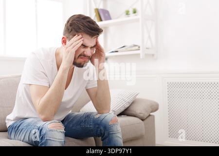 Man Sitting on Couch With Headache in Bright Living Room During Daytime Stock Photo