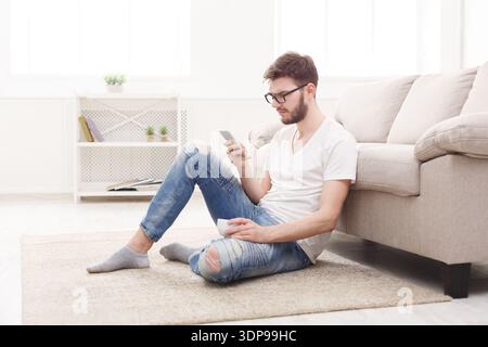 Man Sits on Floor in Living Room and Uses Smartphone During Daytime Stock Photo