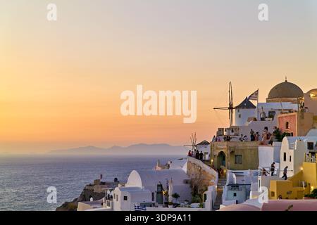Tourists gather on rooftops in Oia, Santorini, Greece, to watch the beautiful sunset over the Aegean Sea, with traditional windmills in view. Stock Photo