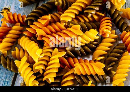 A full-frame, close-up shot of uncooked tricolore fusilli (or rotini) pasta, highlighting the vibrant orange, yellow, and green spiral shapes and deta Stock Photo