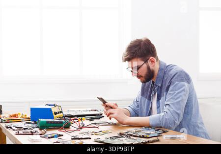 Man Working on Electronics Repair at a Table With Circuit Boards and Tools in a Bright Room Stock Photo